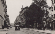 Load image into Gallery viewer, Vintage black and white photograph of a city street with buildings, a car, and pedestrians.