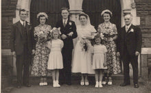 Load image into Gallery viewer, Black and white photograph of a wedding party in front of a building