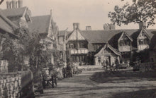 Load image into Gallery viewer, Historic black and white photograph of a row of buildings with a garden and chairs in front.