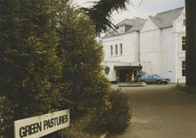 Load image into Gallery viewer, White building with 'Green Pastures' sign in front, surrounded by trees.