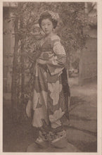 Load image into Gallery viewer, Woman in a traditional kimono standing outdoors with trees and flowers in the background
