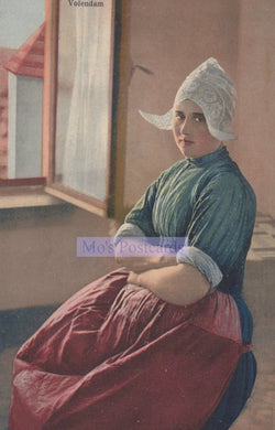 Woman in a red dress and white headscarf sitting by a window, with 'Volendam' text.