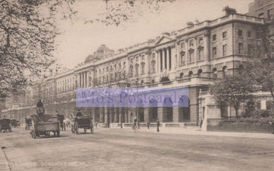 Vintage black and white photo of a city street with horse-drawn carriages and a large building.