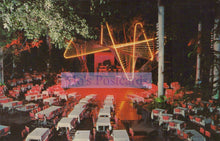 Load image into Gallery viewer, Outdoor event with tables and chairs under a large illuminated sign at night.
