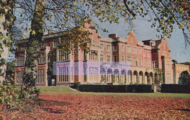 Large brick building with a garden in front, trees with autumn leaves.