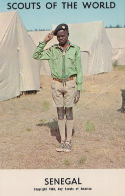 Scout in uniform standing in front of tents with 'Scouts of the World' and 'Senegal' text.