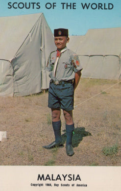 Scout in uniform standing in front of tents with 'Scouts of the World' and 'Malaysia' text.