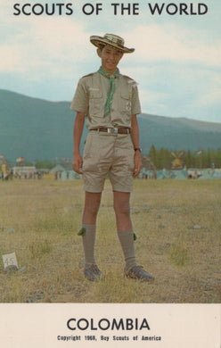 Scout in uniform standing in a field with mountains in the background, labeled 'Scouts of the World, Colombia'.