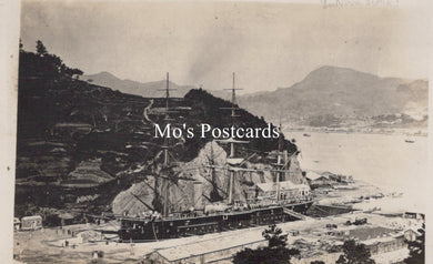 Vintage black and white photograph of a large ship docked at a harbor with mountains in the background  