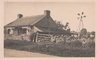 Vintage black and white photo of a house with a windmill in the background