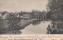 Load image into Gallery viewer, Vintage black and white photograph of a bridge over a river with trees and buildings in the background.
