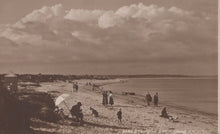Load image into Gallery viewer, Vintage sepia-toned photograph of a beach scene with people and umbrellas under a cloudy sky.
