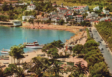 Coastal town with a harbor and beach, featuring buildings and a boat.