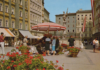 Vintage street scene with people, umbrellas, and flowers in a European city.