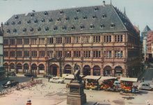 Load image into Gallery viewer, Historic building with a statue in a city square, vintage cars and people around
