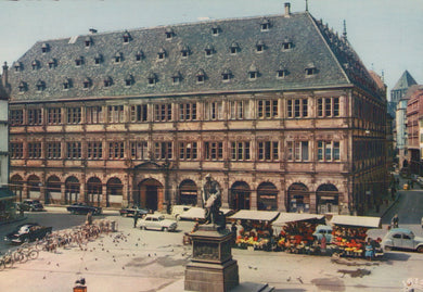 Historic building with a statue in a city square, vintage cars and people around