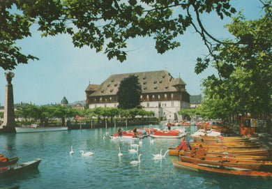 Historic building by a lake with boats and swans on a sunny day