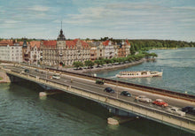 Load image into Gallery viewer, Bridge over a river with cars and a boat, buildings on the opposite bank
