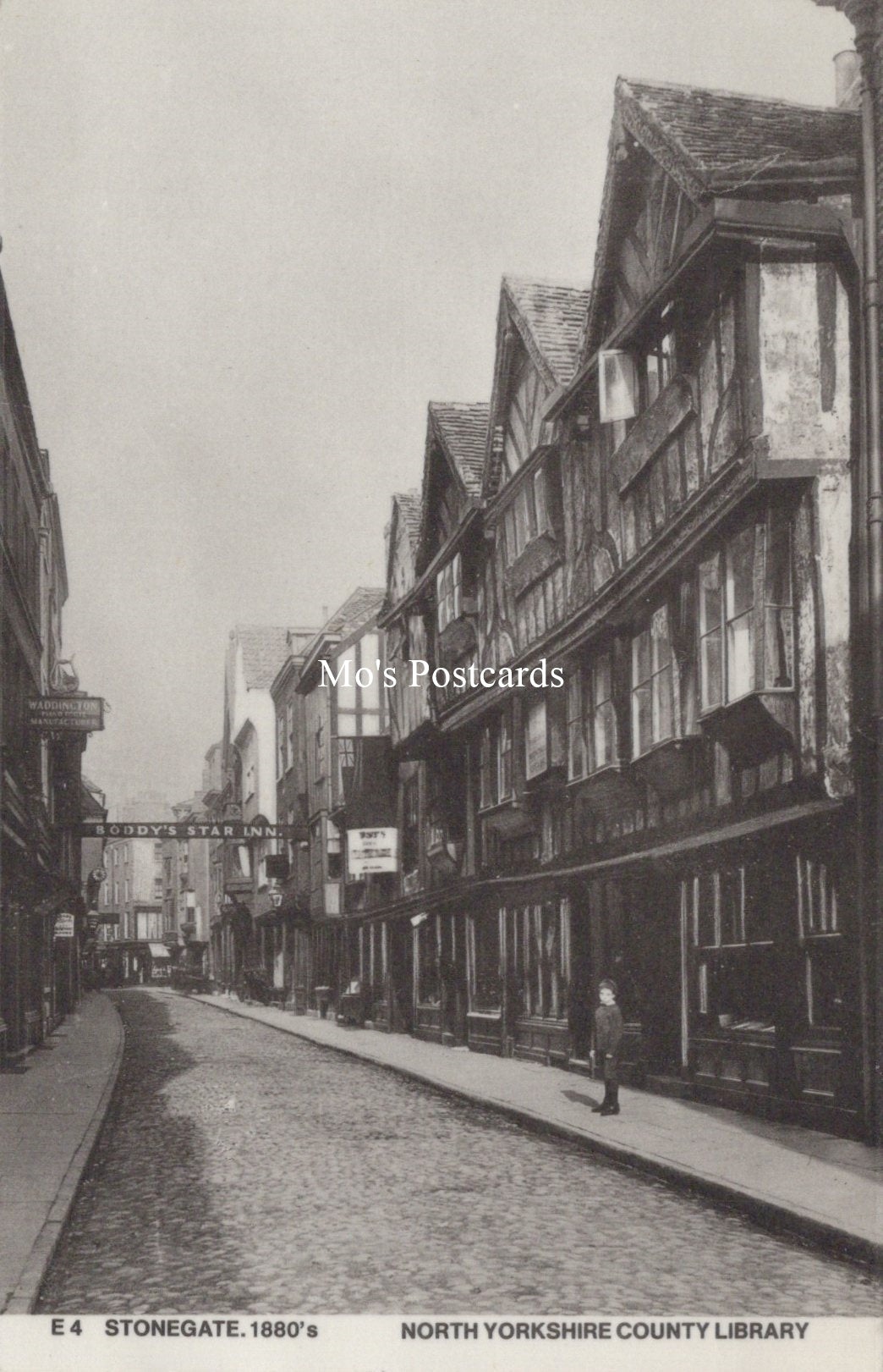 Vintage black and white street scene with traditional buildings and a person walking on a cobbled street.
