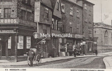 Load image into Gallery viewer, Vintage black and white photograph of a street scene with shops and a horse-drawn carriage 
