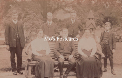 Vintage sepia-toned photograph of a group of people sitting on a bench outdoors.