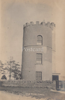 Round tower with crenellated top, stone wall, and trees in the background on a postcard.