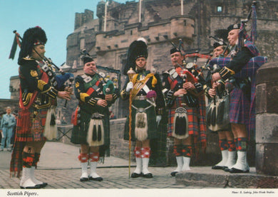 Group of Scottish pipers in traditional dress standing in front of a castle.