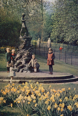 Children playing around a statue in a park with yellow flowers in the foreground.