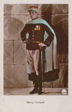 Man in formal military uniform with cape and hat, standing against a stone wall.