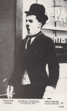 Black and white image of Charlie Chaplin with a top hat and bow tie, sitting on a bench.