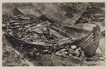 Load image into Gallery viewer, Wrecked wooden boat on a rocky shore with a small hut nearby.
