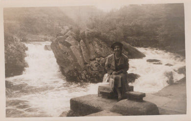 Person sitting on a rock by a flowing stream with a mountainous background