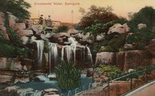 Load image into Gallery viewer, Vintage-style image of a decorative water feature with rocks and people in the background.
