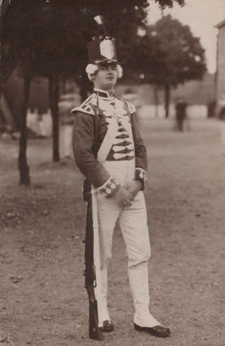 Person in a formal military uniform standing outdoors with trees and grass in the background