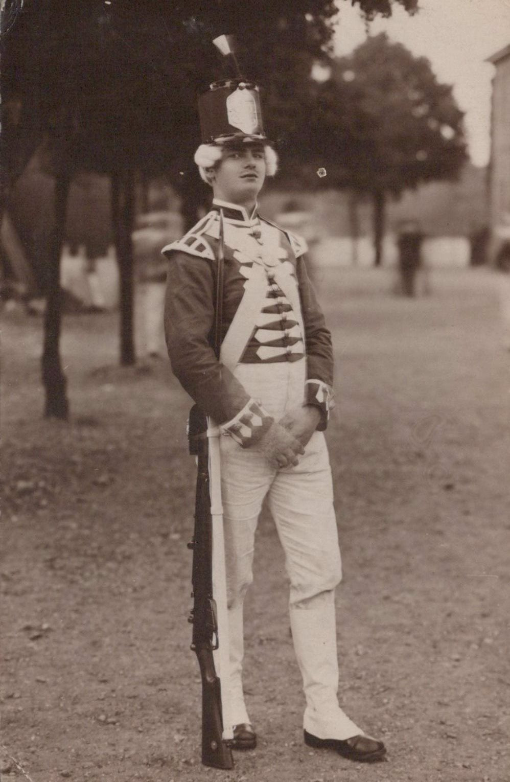Person in a formal military uniform standing outdoors with trees and grass in the background