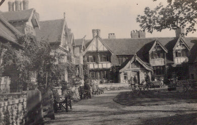 Historic black and white photograph of a row of buildings with a garden and chairs in front.