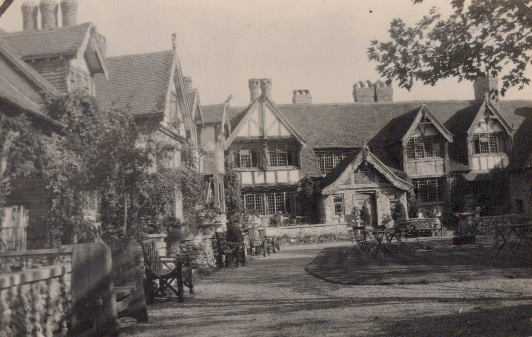 Historic black and white photograph of a row of buildings with a garden and chairs in front.