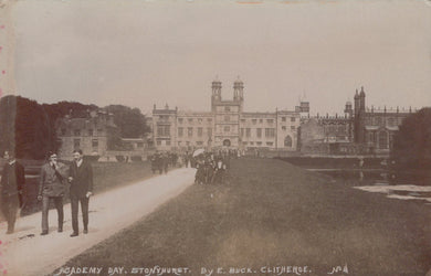 Vintage photograph of a large building with two men walking on a path in front.