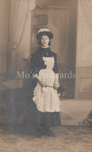 Load image into Gallery viewer, Vintage black and white photograph of a woman in formal attire with a hat, standing indoors.
