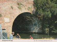 Load image into Gallery viewer, Children playing by a river under Hungerford Bridge with a brick wall and greenery.
