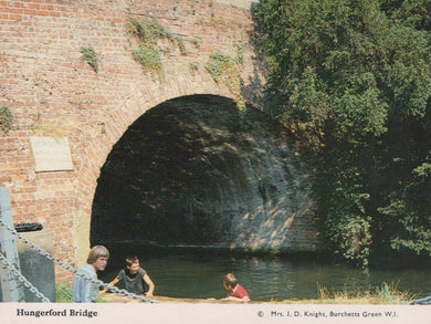 Children playing by a river under Hungerford Bridge with a brick wall and greenery.