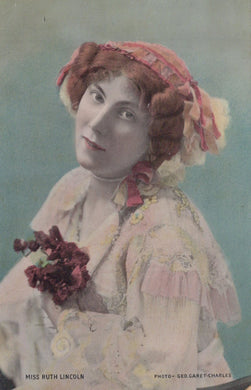 Vintage photograph of a woman in a decorative outfit with a pink bonnet and floral arrangement.