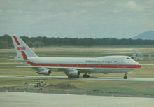 Load image into Gallery viewer, Indonesian Airways airplane on a runway with trees and mountains in the background
