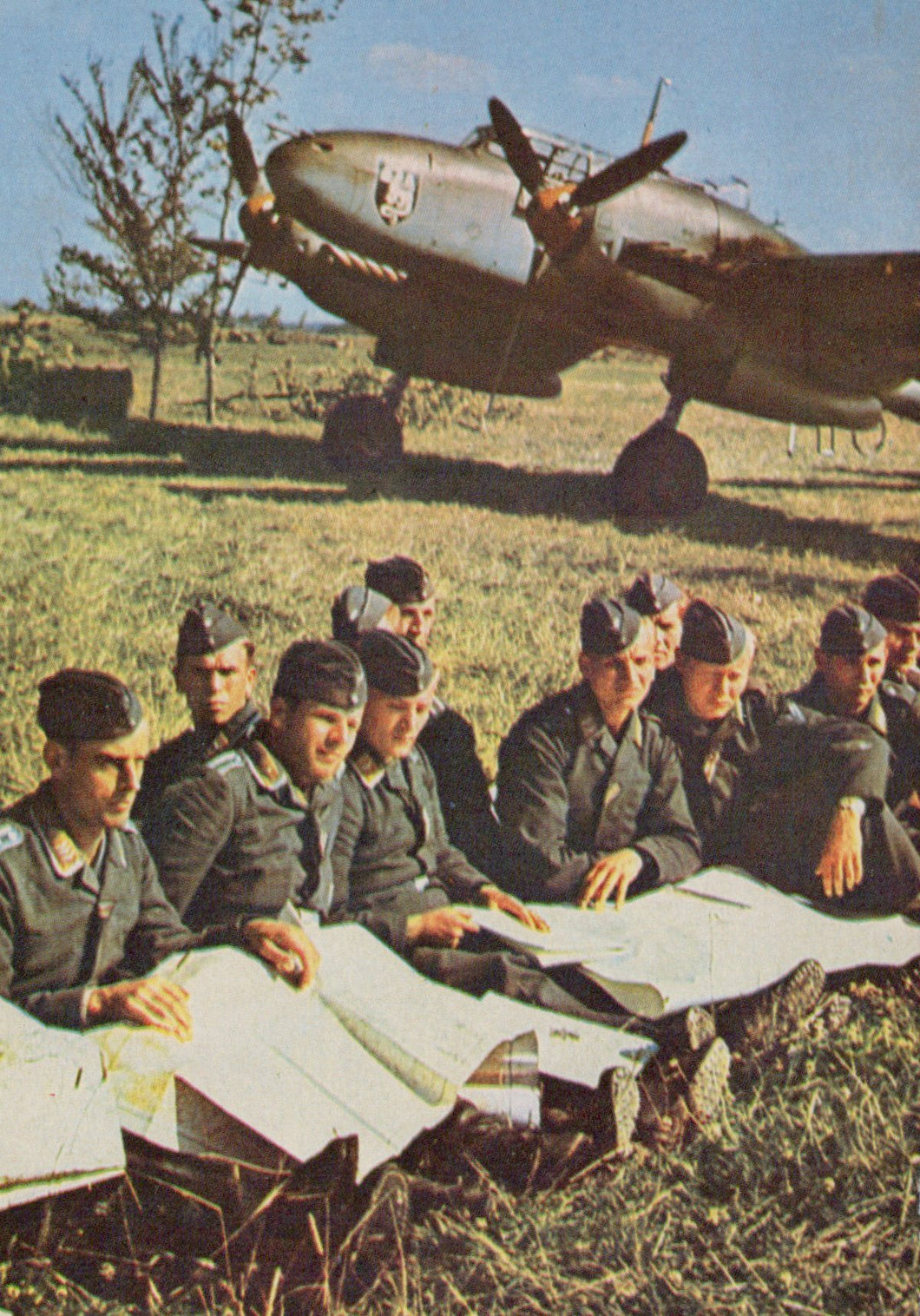 Group of soldiers sitting on the grass with a military aircraft in the background