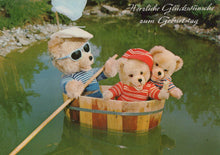 Load image into Gallery viewer, Three teddy bears in a wooden barrel on water with German text above
