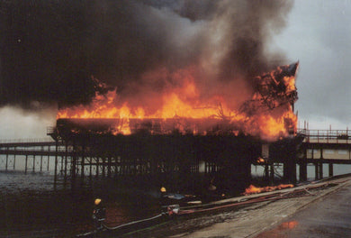 Building on fire with flames and smoke billowing out, near a pier.
