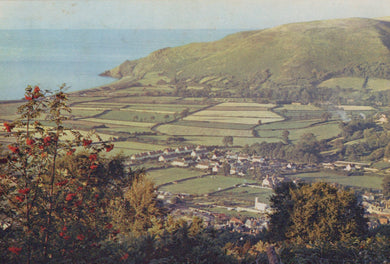 Village nestled in a valley with rolling hills and a body of water in the background