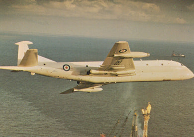 Military aircraft flying over water with a visible logo on the tail.